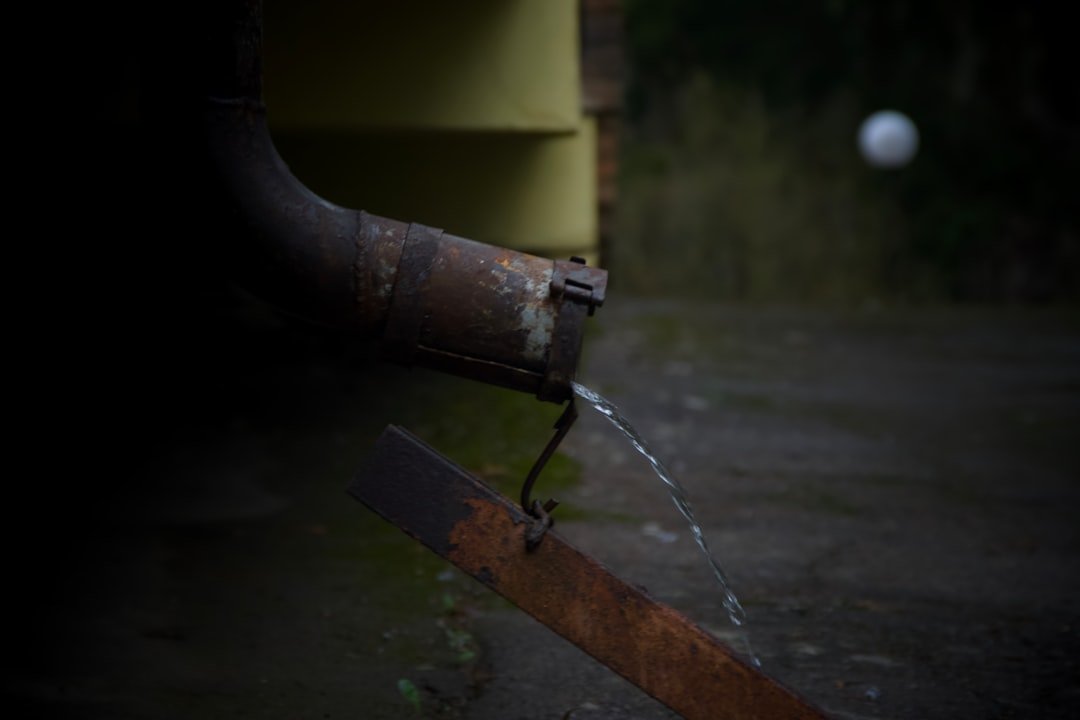 Water dripping from a rusty downspout onto a metal surface